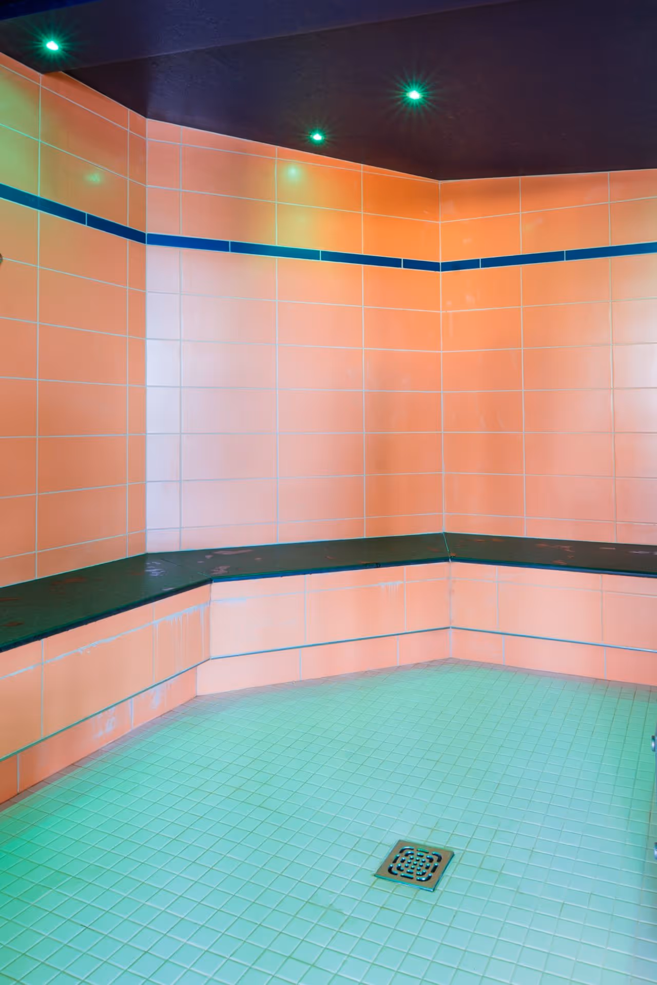 Modernes Duschzimmer mit rosa Kacheln, grünem Boden und grünen Lichtern