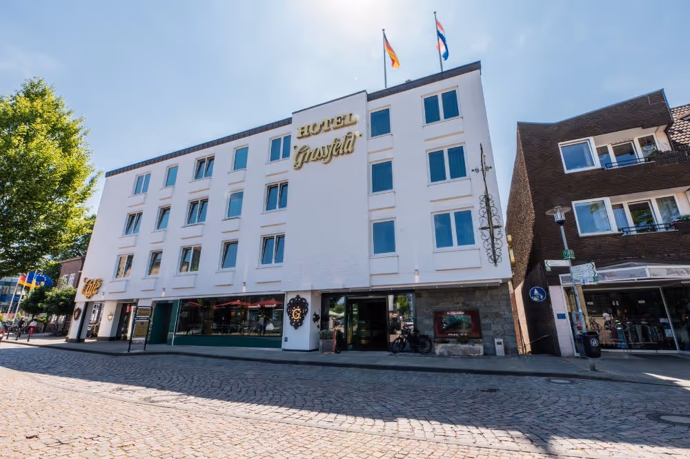 Weißes Hotel Grosfeld mit deutscher und niederländischer Flagge an sonnigem Tag