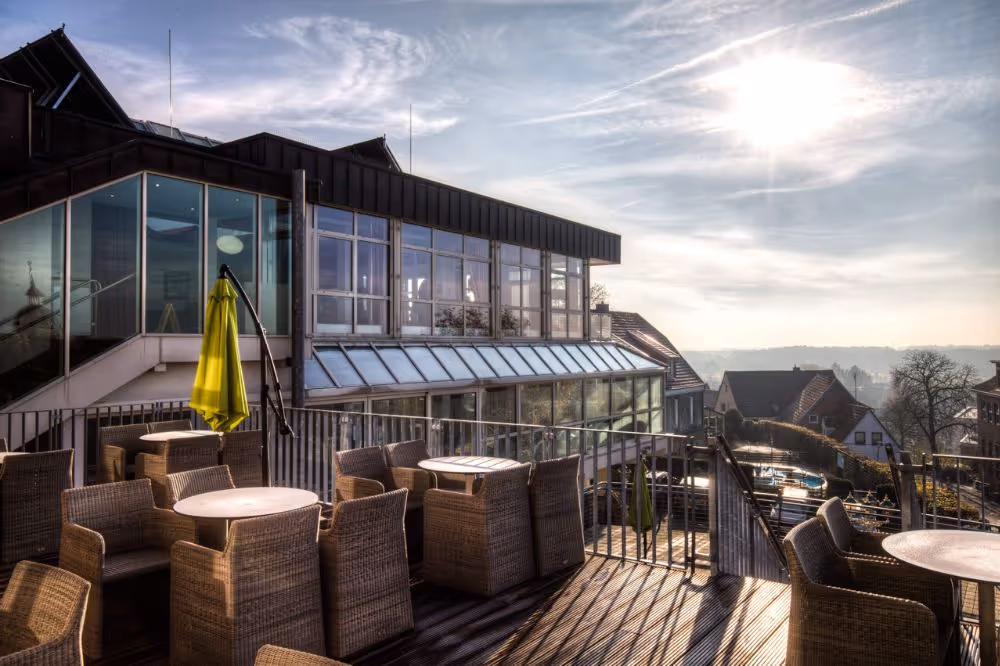 Sonnige Dachterrasse mit Rattanmöbeln und Glasgebäude im Hintergrund
