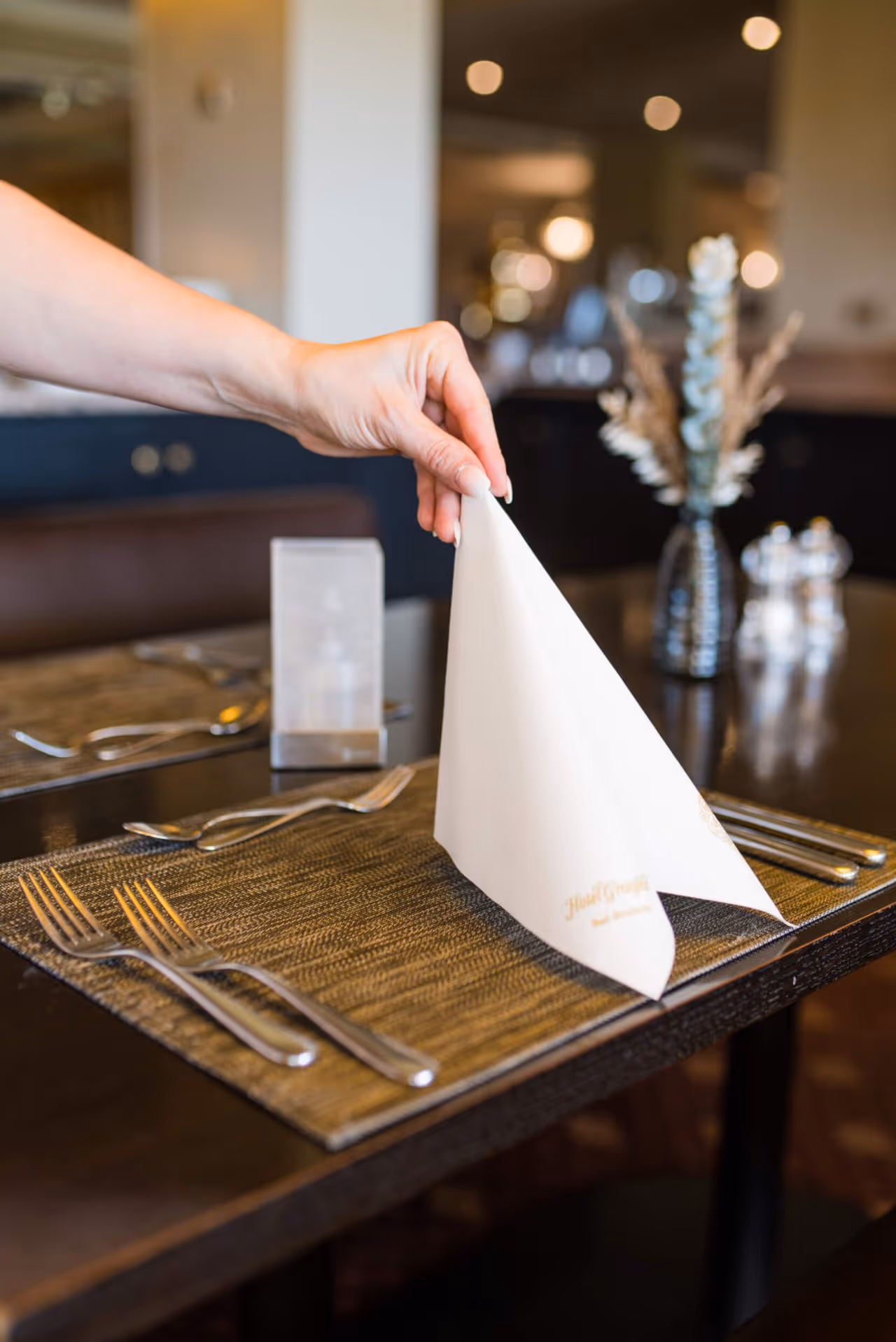 Hand richtet weiße Serviette auf gedecktem Tisch in elegantem Restaurant