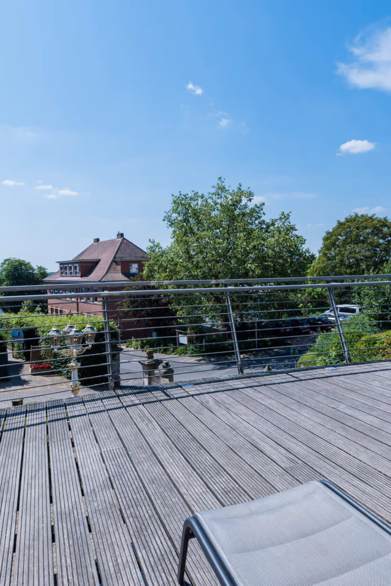 Sonnige Dachterrasse mit Holzdielen, Metallgeländer und Blick auf Gebäude