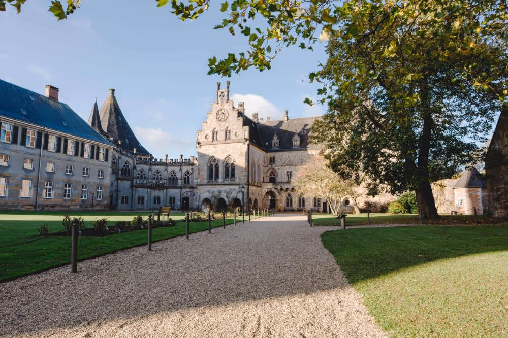 Historisches Schloss mit Uhrenturm und Kiesweg, umgeben von grünem Rasen