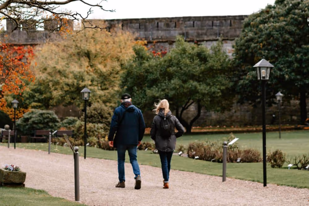 Zwei Personen spazieren im Herbst durch einen gepflegten Park mit Laternen