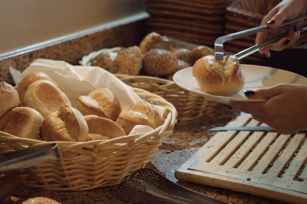Frische Brötchen in Körben, Hand nimmt Brötchen mit Zange