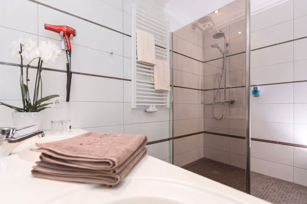 Modernes Badezimmer mit Dusche, Handtüchern und rotem Föhn