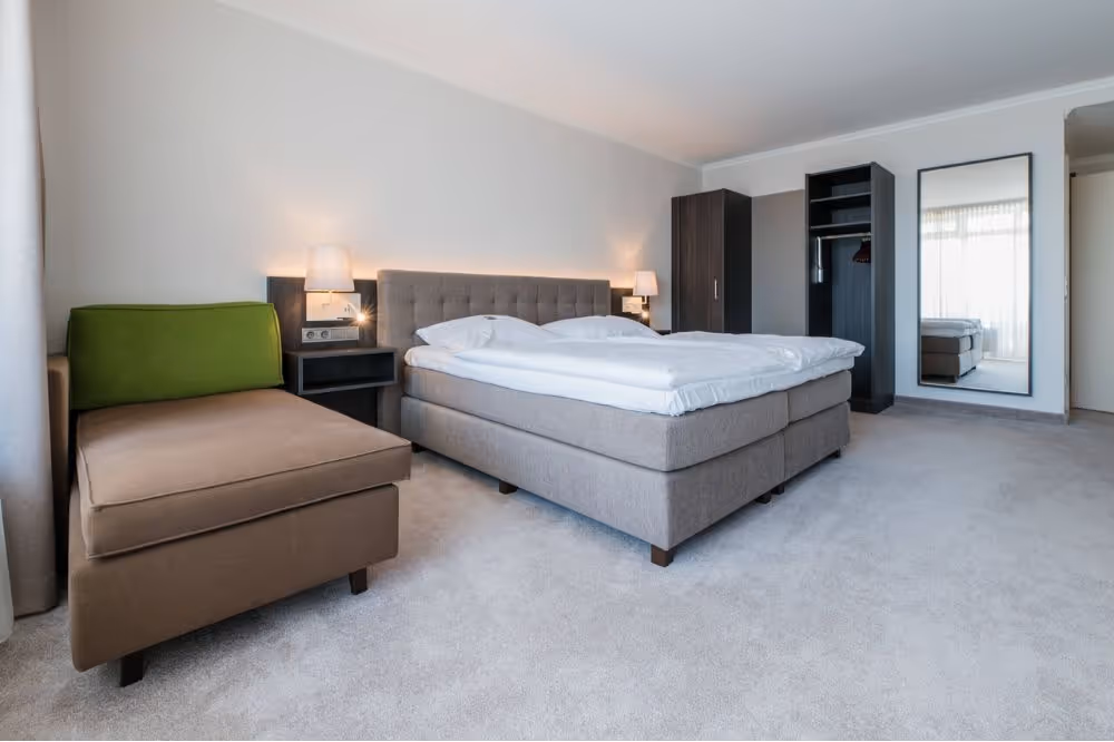 Modernes Hotelzimmer mit grauem Bett, Sessel und offenem Kleiderschrank