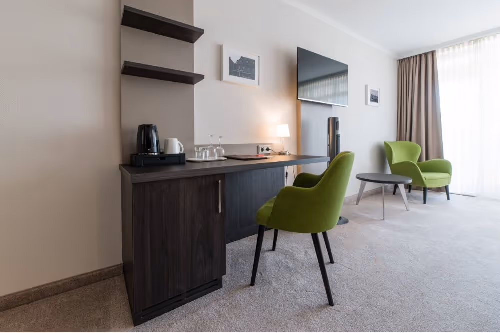 Hotelzimmer mit grünen Sesseln, Kaffeemaschine und Flachbild-TV