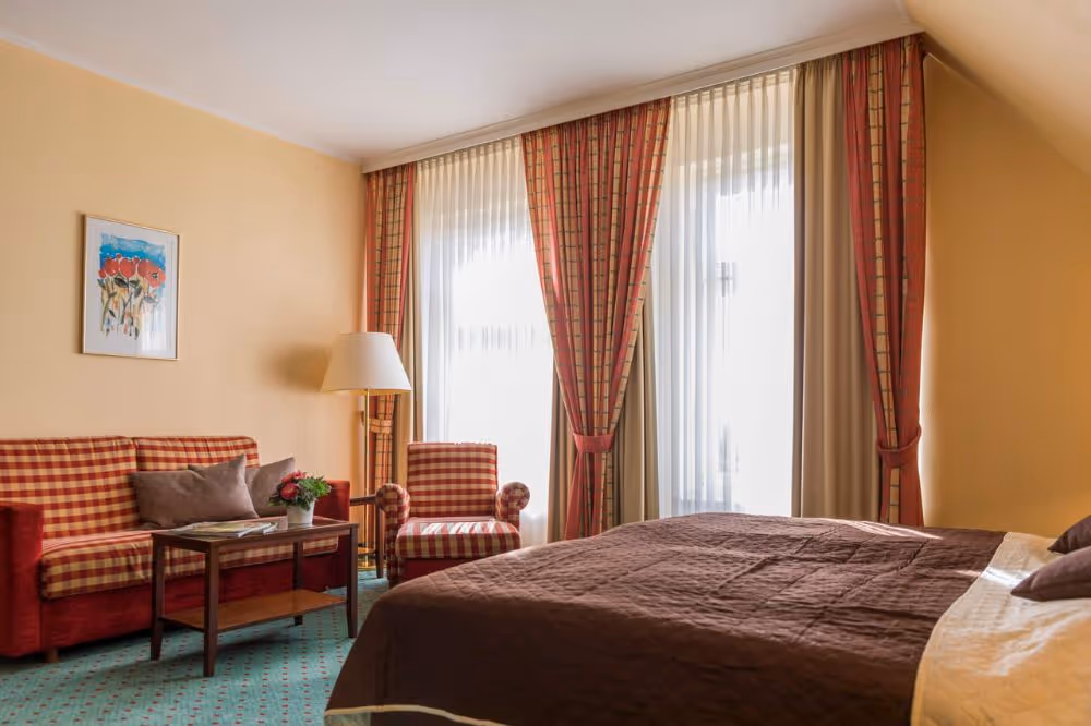 Gemütliches Hotelzimmer mit karierter Couch, Bett und großen Fenstern