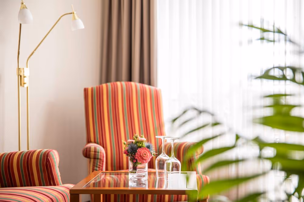 Gestreifte Sessel, Glastisch, Blumen und Stehlampe in hellem Interieur