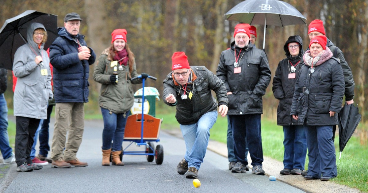 Ältere Menschen spielen bei Regen Boule auf einem Waldweg