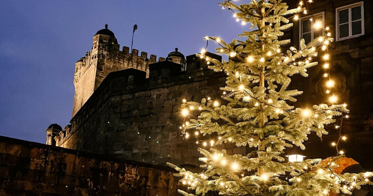 Weihnachtsbaum mit Lichtern vor einer alten Steinburg in der Abenddämmerung