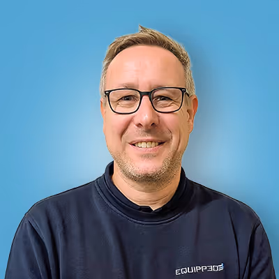 Lächelnder Mann mit Brille und kurzem Haar vor blauem Hintergrund, trägt ein dunkles Sweatshirt mit der Aufschrift ‚EQUIPP365‘.