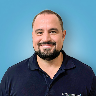 Mann mit kurzem Haar und Bart, der ein dunkles Polohemd mit dem Equippräd-Logo trägt, vor blauem Hintergrund lächelnd.