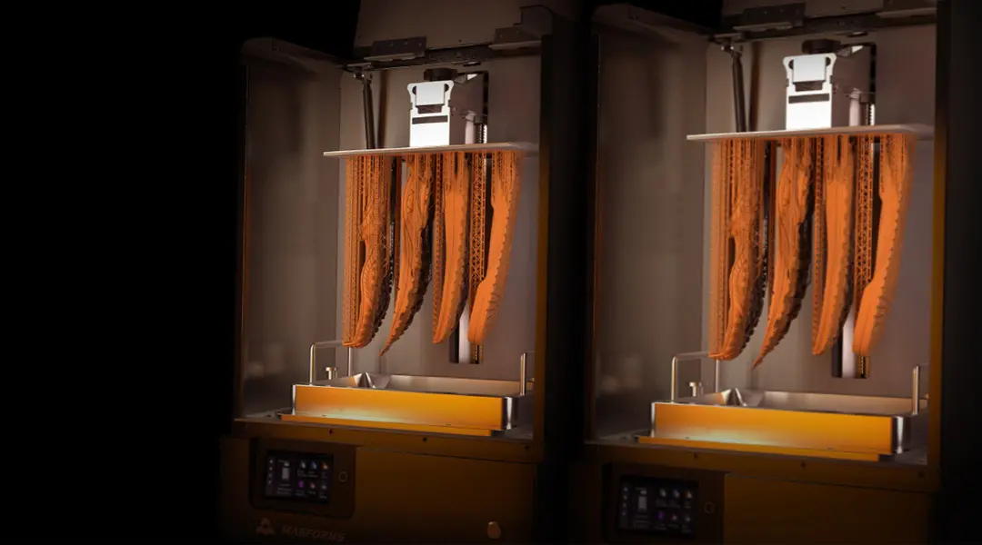 In einem geschlossenen 3D-Drucker hängen fünf orangene, komplex geformte 3D-gedruckte Teile zum Aushärten.