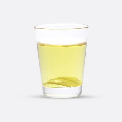 Glas mit hellgelbem Wasser und einem Teebeutel darin.