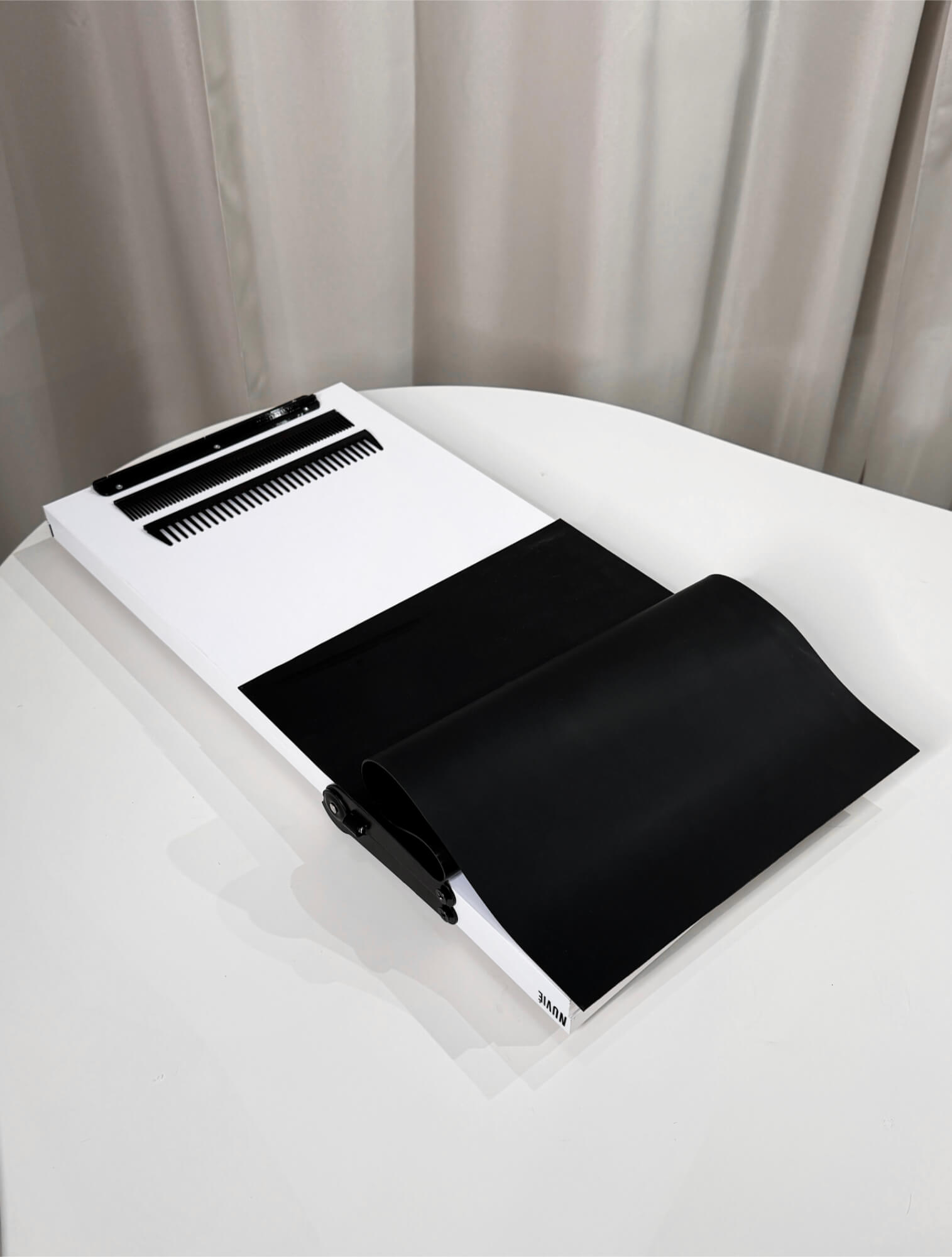 Black and white clipboard with black combs attached on a white table.