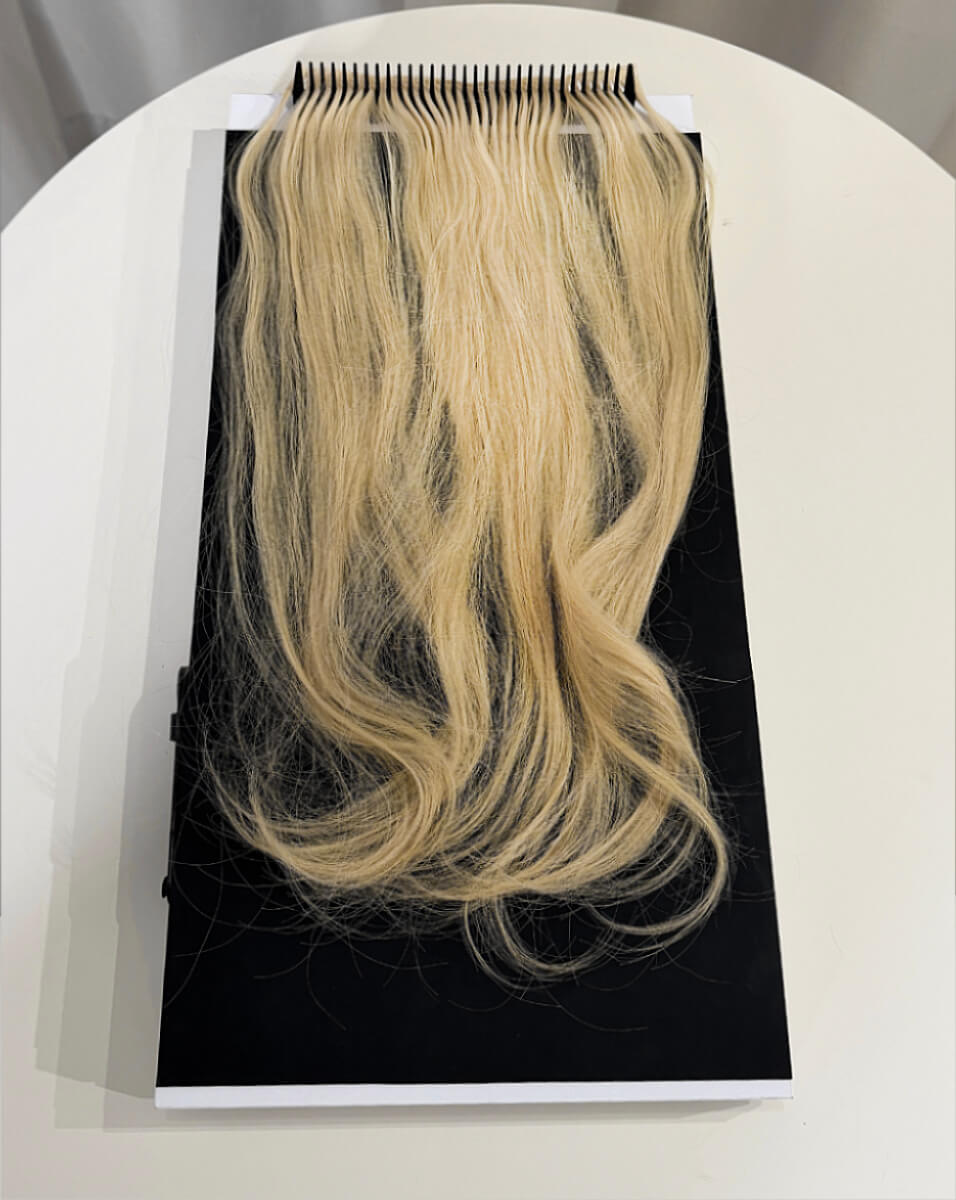 Blonde hair extensions attached to a black comb laid flat on a white surface.