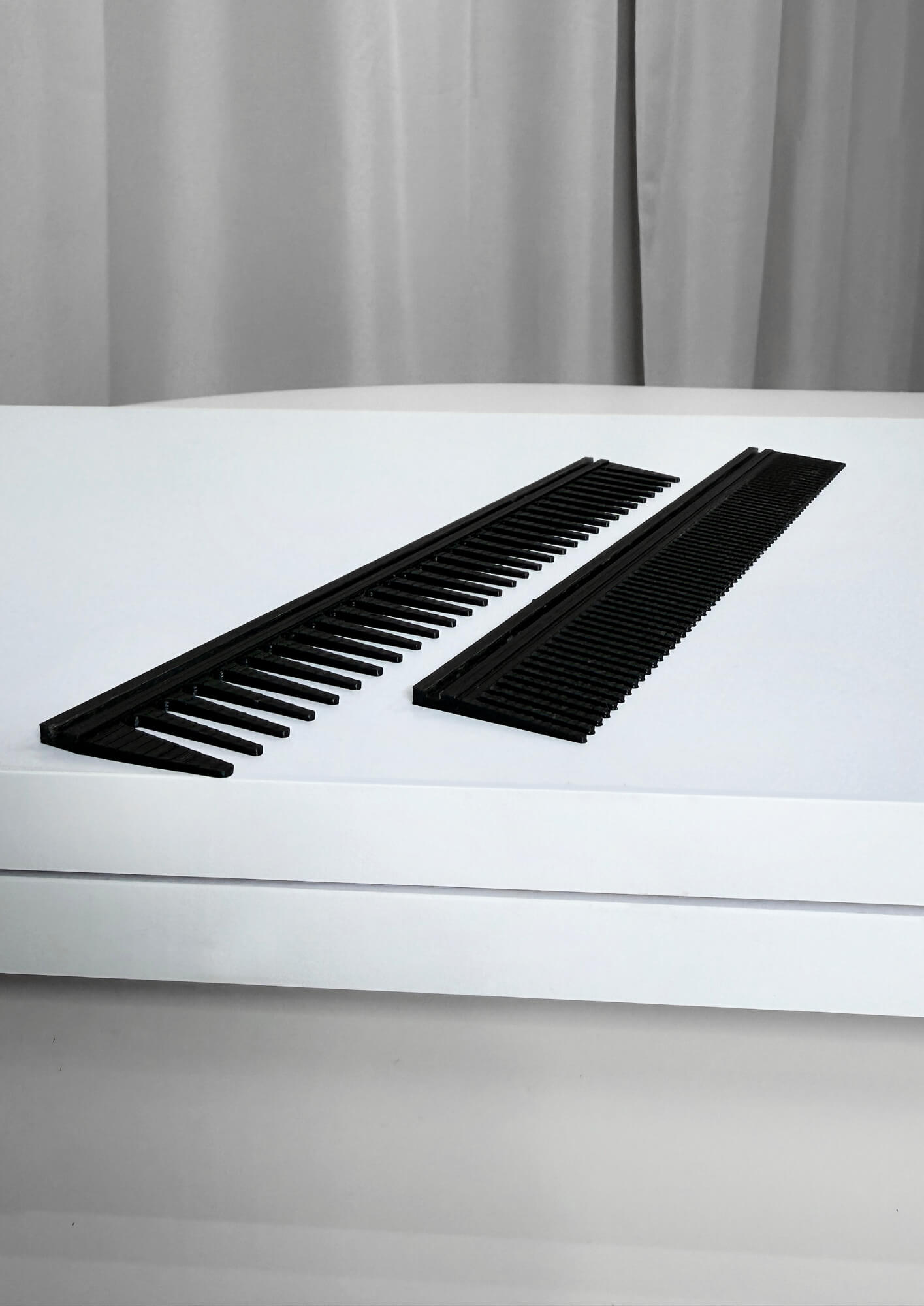 Two black hair combs placed parallel on a white surface in front of gray curtains.