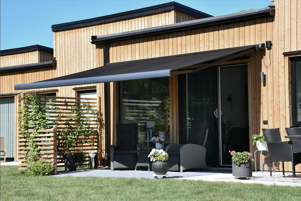 Trädgård med gräsmatta och modern träfasad på hus med svart terrassmarkis och utemöbler i Stockholm.