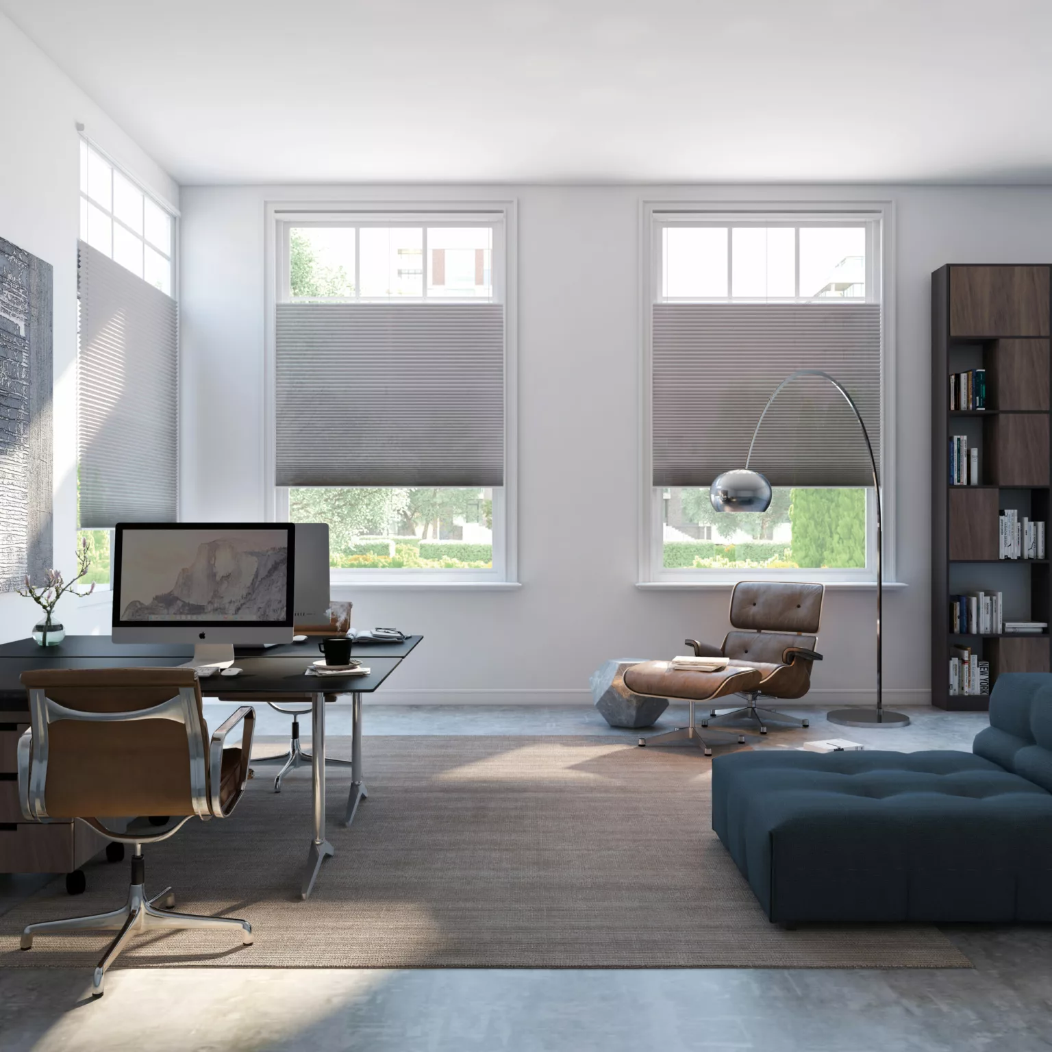 Modernt hemmakontor med skrivbord, dator, kontorsstol, läsfåtölj, golvlampa, bokhylla och stor blå soffa med plisségardiner i fönstren i Stockholm.