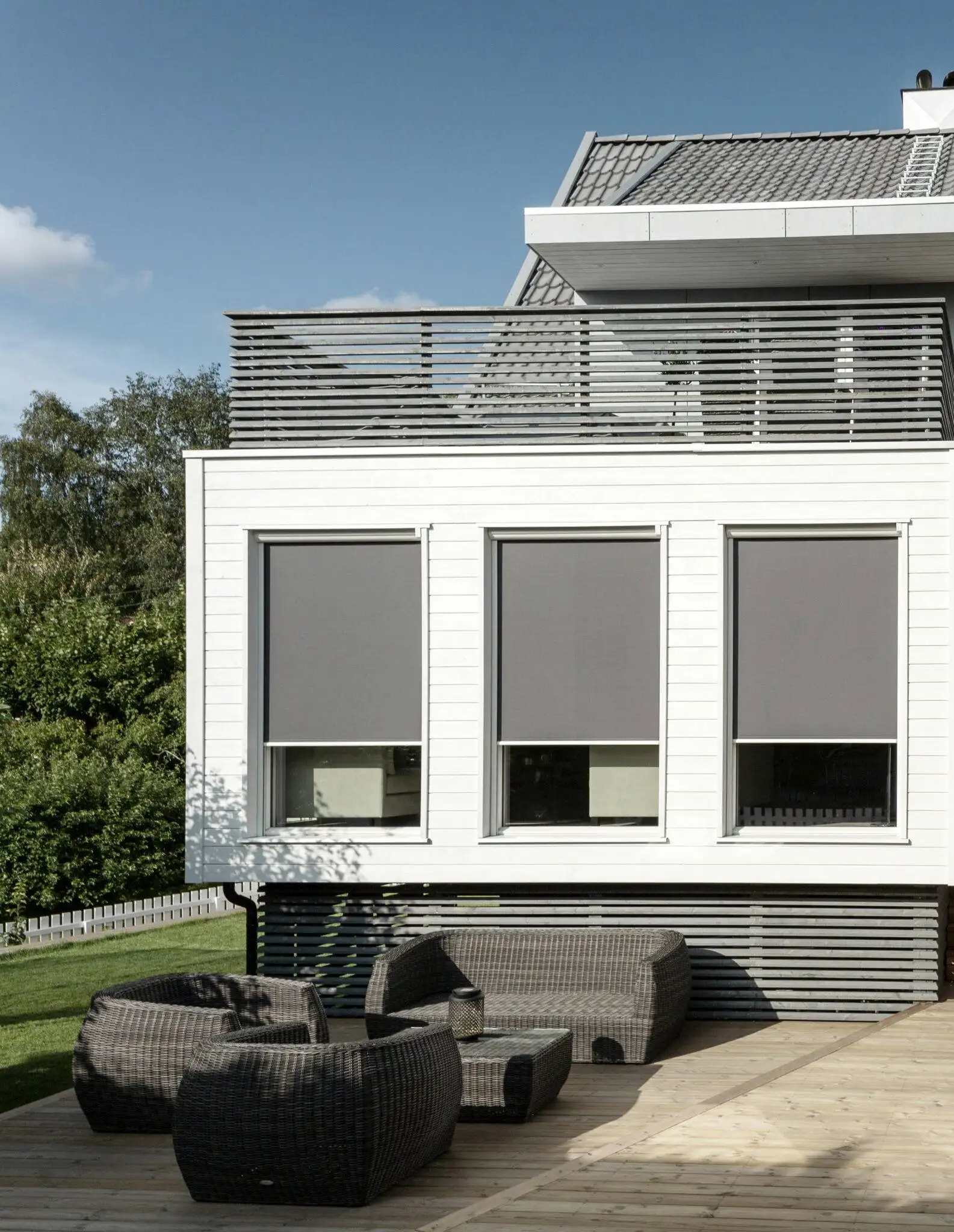 Vit modern husfasad med tre gråa zipscreens z360 och utemöbler i rotting på träaltan i Stockholm.