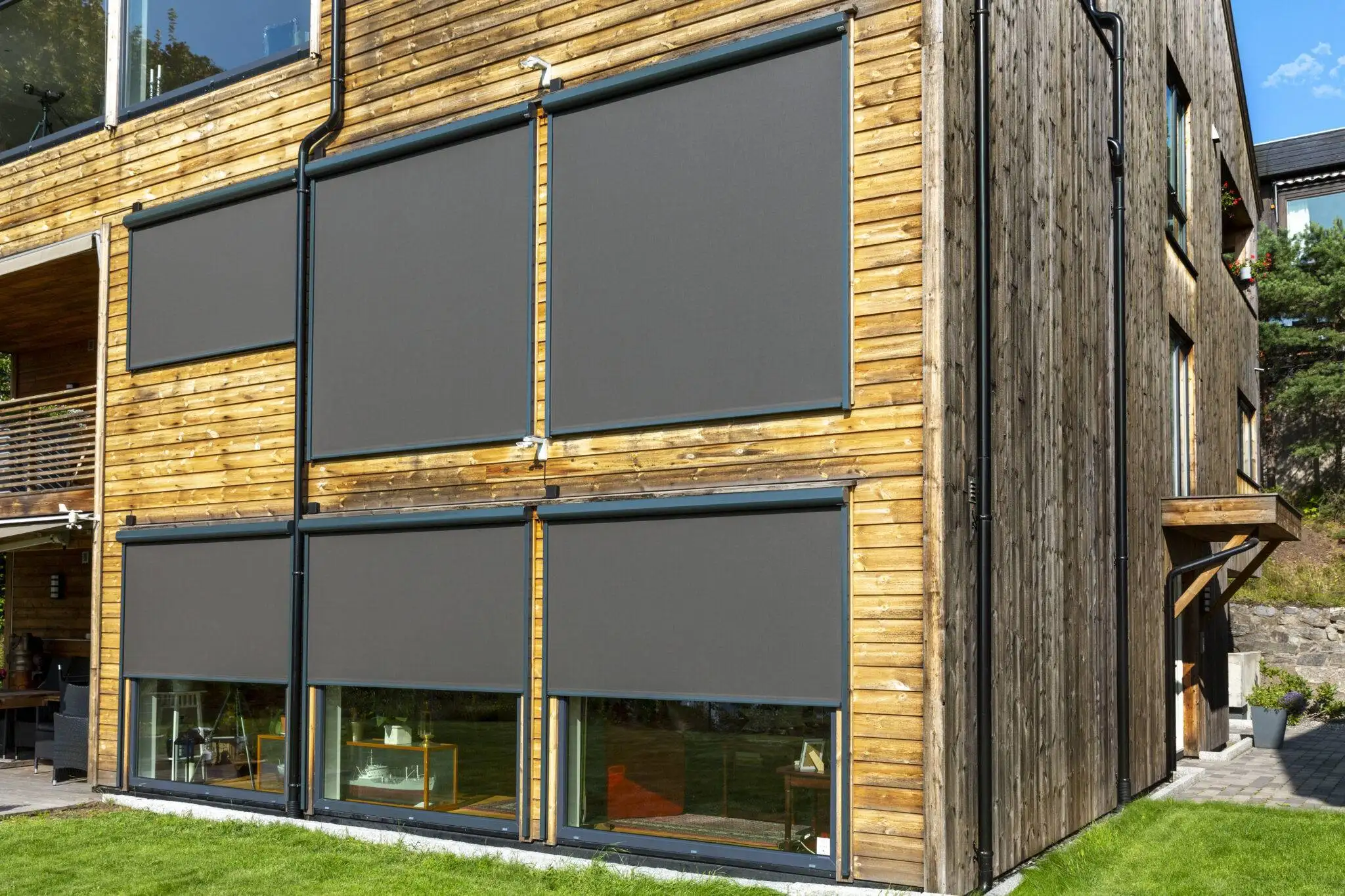 Trähus med fem stora fönster täckta av gråa zipscreens Z460 på en gräsmatta i Stockholm.