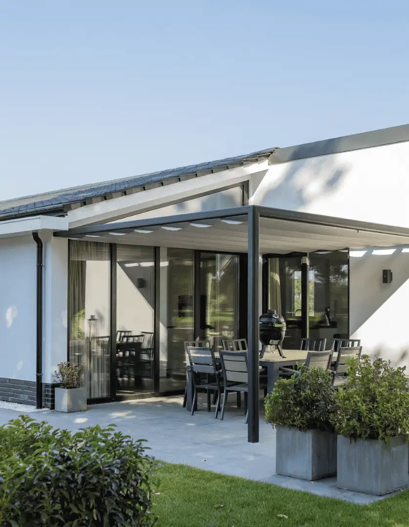 Modern vit utomhus uteplats med svart pergola Sundaze och trädgårdsmöbler i en trädgård med gräs och buskar i Stockholm.