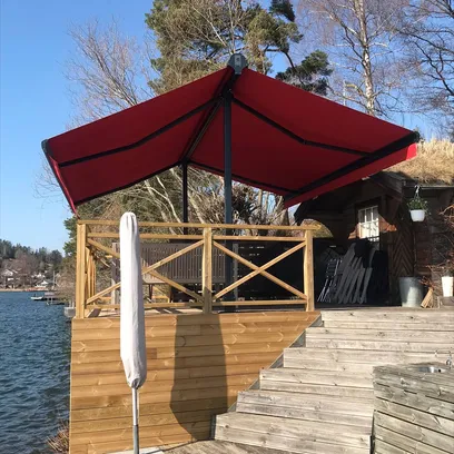 Röd terrassmarkis Duo och träaltan vid vattnet i solsken med trappor och träd i bakgrunden i Stockholm.