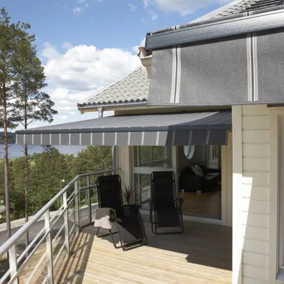 Uteplats med två svarta solstolar under en grå randig terrassmarkis T420, med utsikt över träd och en sjö i bakgrunden i Stockholm.