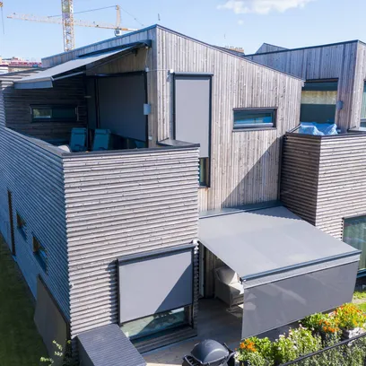 Modernt radhus med träfasad, markiser och möblerade uteplatser med växter i Stockholm.