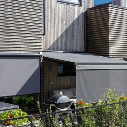 Terrass med markiser i grått på ett modernt trähus med utemöbler och en grill i Stockholm.
