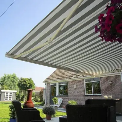 Trädgård med möblerad uteplats med randig terrassmarkis T720 ovanför och ett hus i bakgrunden i Stockholm.