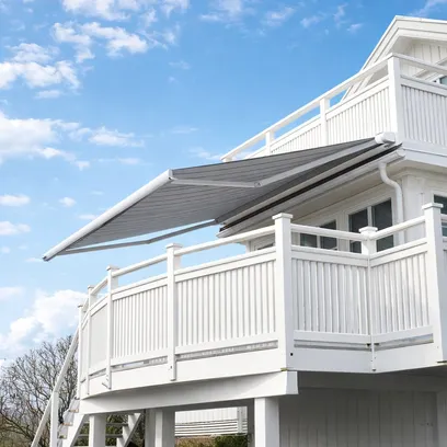 Vit träveranda med utsträckt mörkgrå terrassmarkis T720 på husets övre våning under en blå himmel med moln i Stockholm.