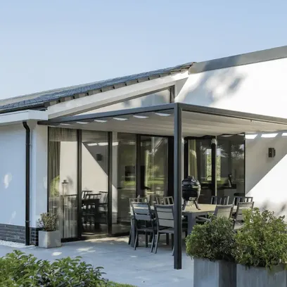 Modern vit utomhus uteplats med svart pergola Sundaze och trädgårdsmöbler i en trädgård med gräs och buskar i Stockholm.