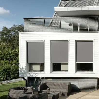 Modern vit byggnad med tre stora fönster med gråa zipscreens Z360 och utemöbler i rotting på träaltan i Stockholm.