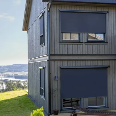 Hörna av tvåvåningshus med utvändiga mörka zipscreens Z460 framför fönstren och gräsmatta runt huset i Stockholm.