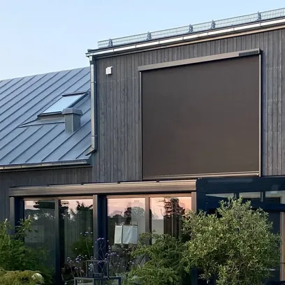 Modernt hus med mörk träfasad, stora fönster och en nedrullad mörk zipscreen Z460 4K på övervåningen, med en pool och växter i förgrunden i Stockholm.