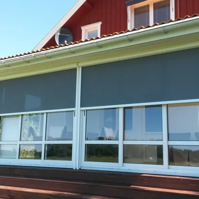 Fönster med neddragna mörkgrå zipscreens Z560 på en röd träbyggnad med vita knutar och trappsteg i trä framför i Stockholm.