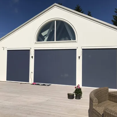 Vit byggnad med tre stora fönster täckta av mörkblå markiser och ett halvmånefönster ovanför.