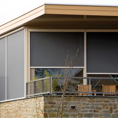 Balkong med stenmur, glasräcke och uteplats som har två trästolar och mörkgråa zipsceens Z560 på fönstren.