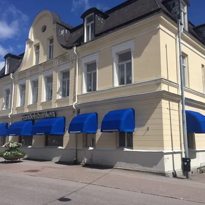 Gammal gul byggnad med blå korgmarkiser K200 och skylt för Handelsbanken under en klarblå himmel i Stockholm.