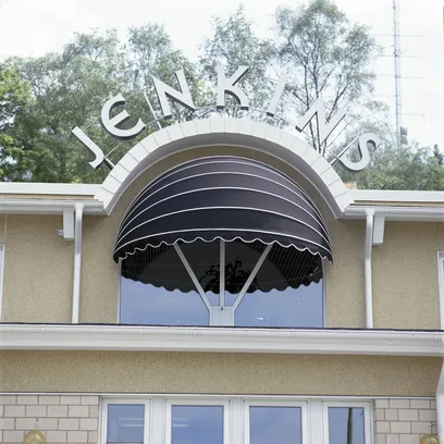 Byggnadsfasad med svart korgmarkis  K200 över bågformat fönster och bokstäverna JENKINS ovanför i Stockholm.