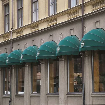 Fasaden av en äldre byggnad med sex gröna korgmarkiser K200 över fönstren i Stockholm.