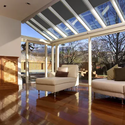 Ljust vardagsrum med glasväggar och tak, trägolv och två vita soffor med kuddar och gråa takzippar TZ330 i Stockholm.