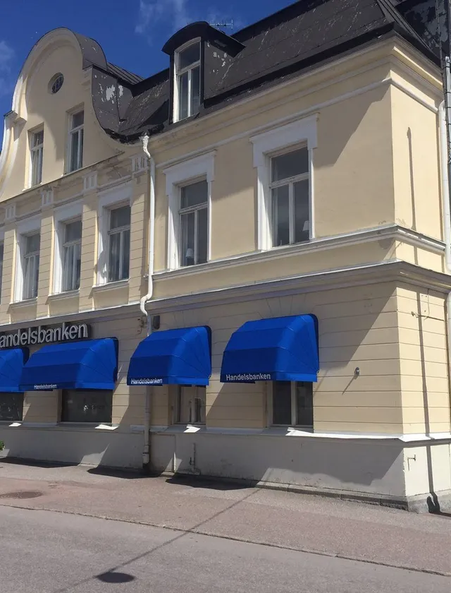 Gammalt beige byggnad med blå markiser och texten Handelsbanken på fasaden.