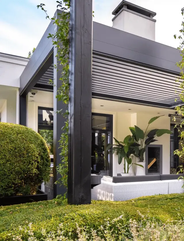 Modern utomhus lounge med svart pergola Arezzo, vita soffor och stora gröna växter runt grönskande trädgård i Stockholm.