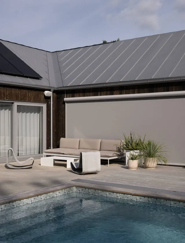 Modern uteplats med pool, beige soffa med småbord och två svängda stolar på träaltan med växter och en nedrullad Styra zipscreen på husets fasad i Stockholm.