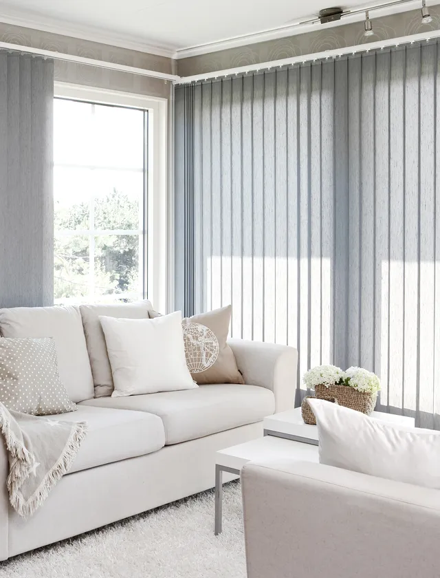 Ljust vardagsrum med gråa lamellgardiner, beige soffa med kuddar och ett litet bord med blommor i Stockholm.