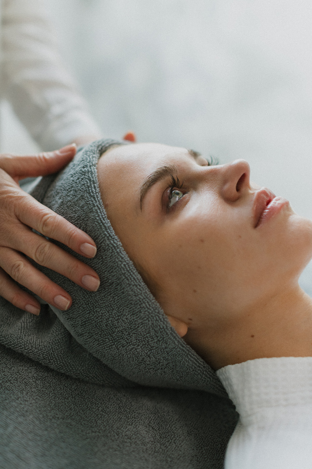 Frau liegt entspannt mit grauem Handtuch um den Kopf, während ihre Haut gepflegt wird.