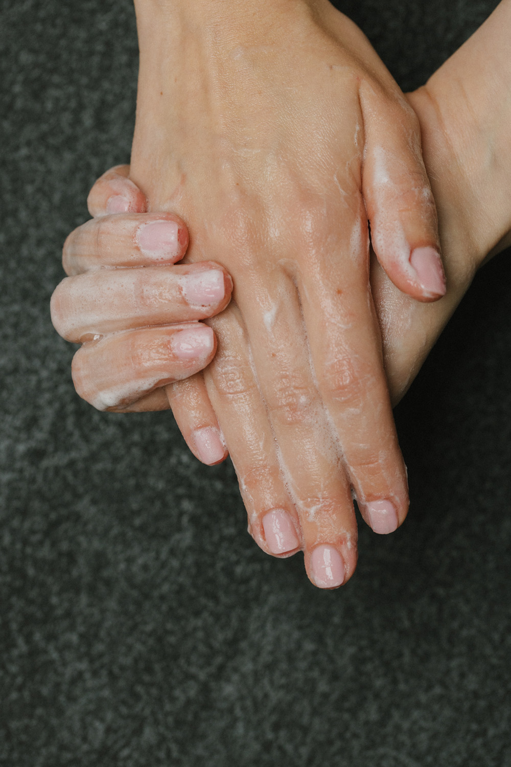 Zwei Hände mit Seifenschaum gründlich waschend auf dunklem Untergrund.